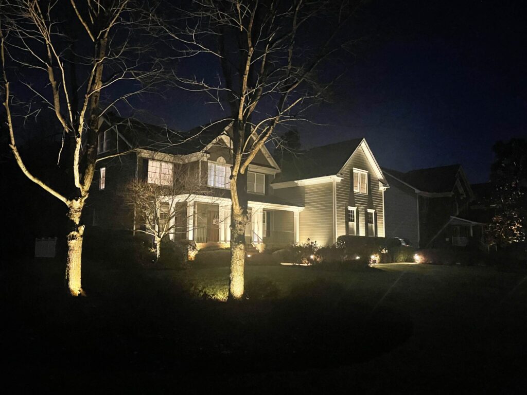 A home and nearby trees illuminated at night