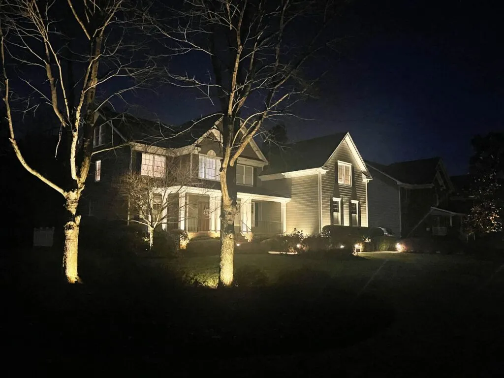 A home and nearby trees illuminated at night